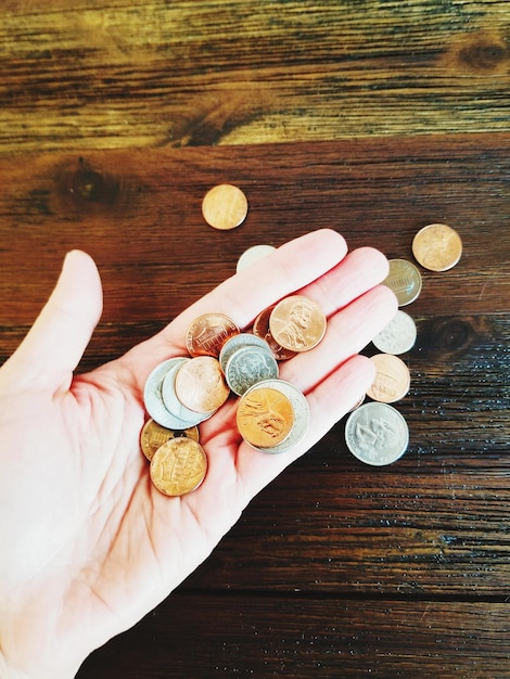 A close-up of a hand holding various coins and currency, with a blurred background showing rising prices on grocery store shelves, visually representing the eroding purchasing power of money due to inflation.
