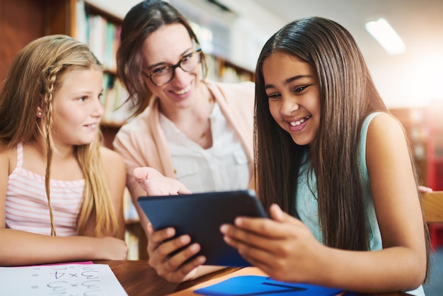 A teacher sits with a student, reviewing a personalized learning plan on a tablet, while other students in the background engage in various learning activities.