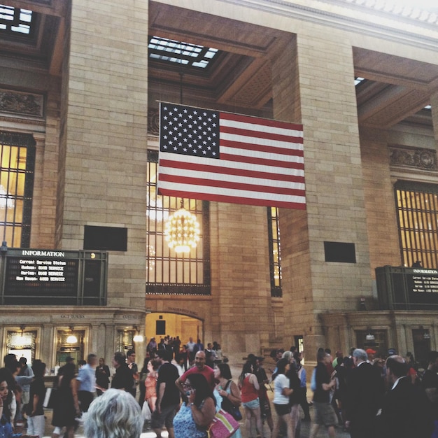 A close-up shot of the Federal Reserve building in Washington D.C., with a blurred background of people walking. The focus is on the building's architecture and the American flag waving in front.